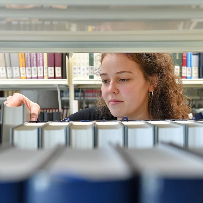 Eine junge Frau sortiert Bücher in ein Regal