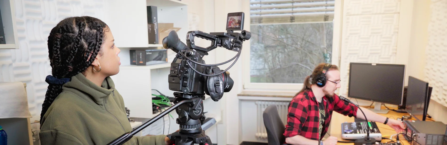 Person bedient professionelle Videokamera auf Stativ in einem Tonstudio mit Schalldämmung
