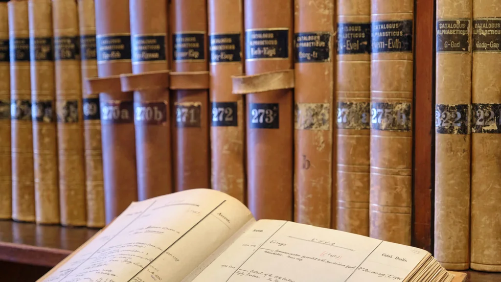 Historische Bibliothekskataloge aus Göttingen Im Hintergrund Bibliothekskataloge auf einem Regal, im linken vorderen Bereich ein aufgeschlagener Bibliothekskatalog