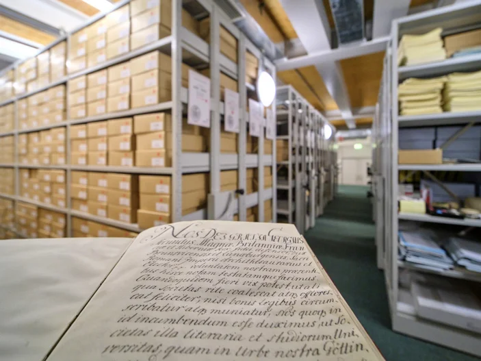 Gründungsurkunde der Universität Göttingen im Vordergrund, dahinter Regale mit Archivalien