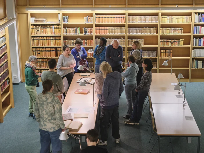 Ein Vortrag vor historischen Büchern, dem eine Gruppe von Menschen aufmerksam folgt