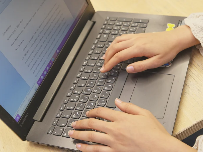 Eine Person arbeitet am Laptop. Auf dem Bildschirm ist eine Textdatei geöffnet.