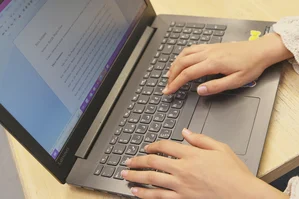 Eine Person arbeitet am Laptop. Auf dem Bildschirm ist eine Textdatei geöffnet.