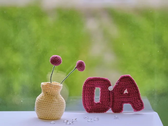 Gehäkeltes OA-Symbol und Blumenwase auf grünen Hintergrund